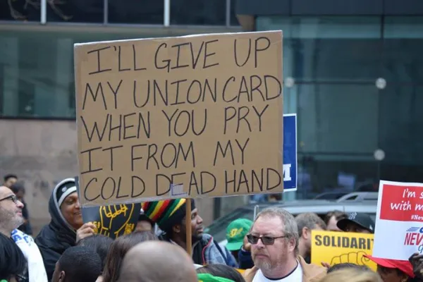 man holding sign in a crowd that says "i'll give up my union card when you pry it from my cold dead hand"
