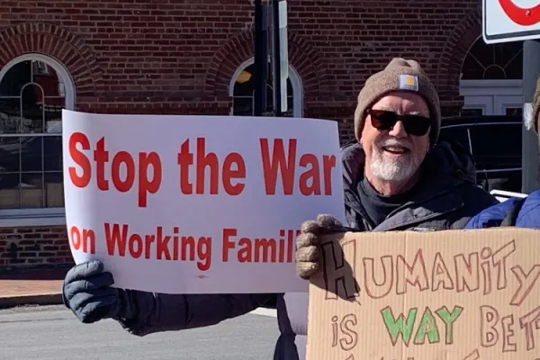 man holding sign that says "stop the war on working families"