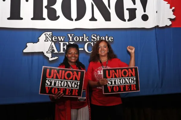 two delegates posing at nys afl-cio convention with "union strong voter" signs