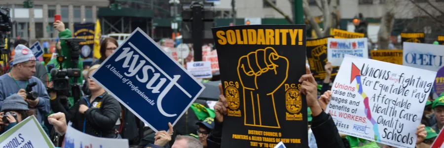 Union members standing in a crowd outside holding signs