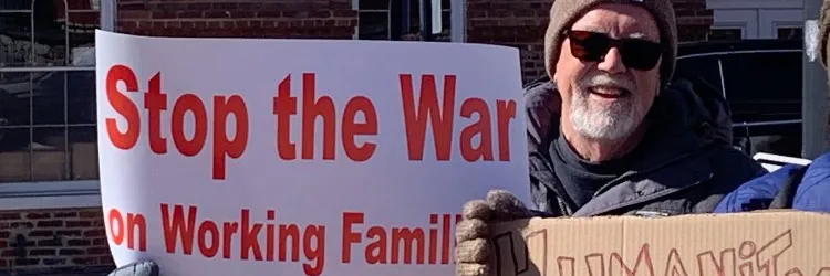 man holding sign that says "stop the war on working families"