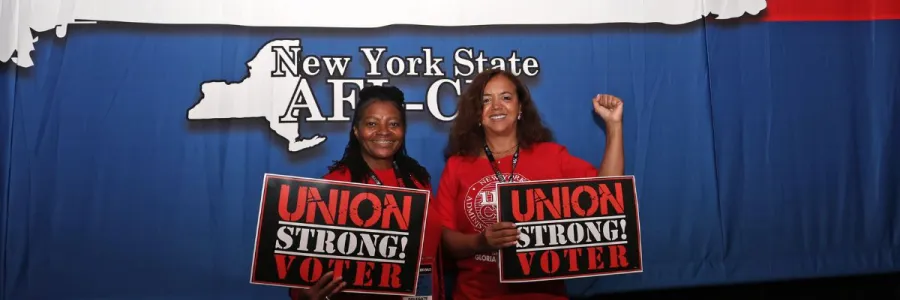 two delegates posing at nys afl-cio convention with "union strong voter" signs