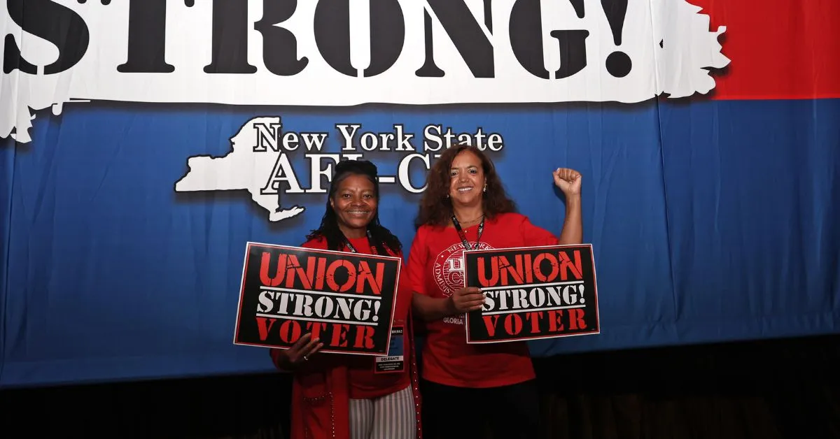 two delegates posing at nys afl-cio convention with "union strong voter" signs